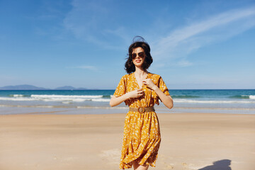 Woman in a bright yellow dress standing on sandy beach with ocean waves in background on sunny day