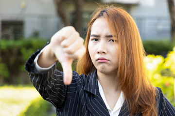 Angry upset Asian office worker woman shows rejecting thumb down gesture, concept image for bad...