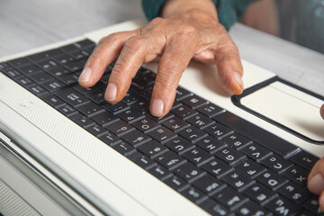 Hands of elderly woman typing in computer keyboard.