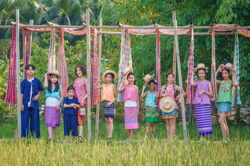 Agriculture organic rice field farm for health. Happy Asian Thai group of boys and girls wear traditional colorful farmer outfits walking on a beautiful green rice field in Thailand. - Powered by Adobe