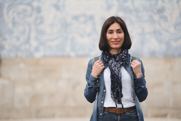 Portrait of female tourist standing with scarf and backpack smiling looking at camera near church...