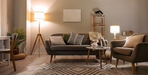 Interior of living room with cozy grey sofa, armchair and glowing lamps