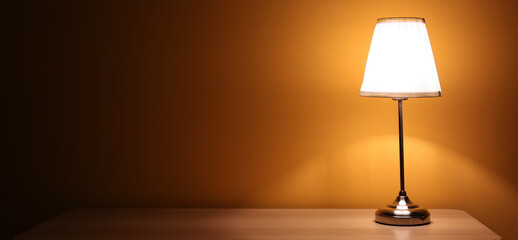 Glowing lamp on wooden table in dark room