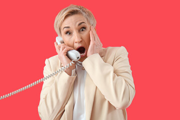 Shocked mature woman talking by telephone on red background