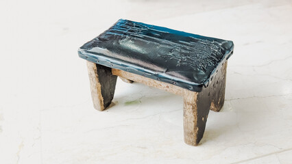 High angle view of a rustic small wooden stool covered by upper wrinkled black leather