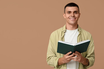 Handsome young man reading book on beige background