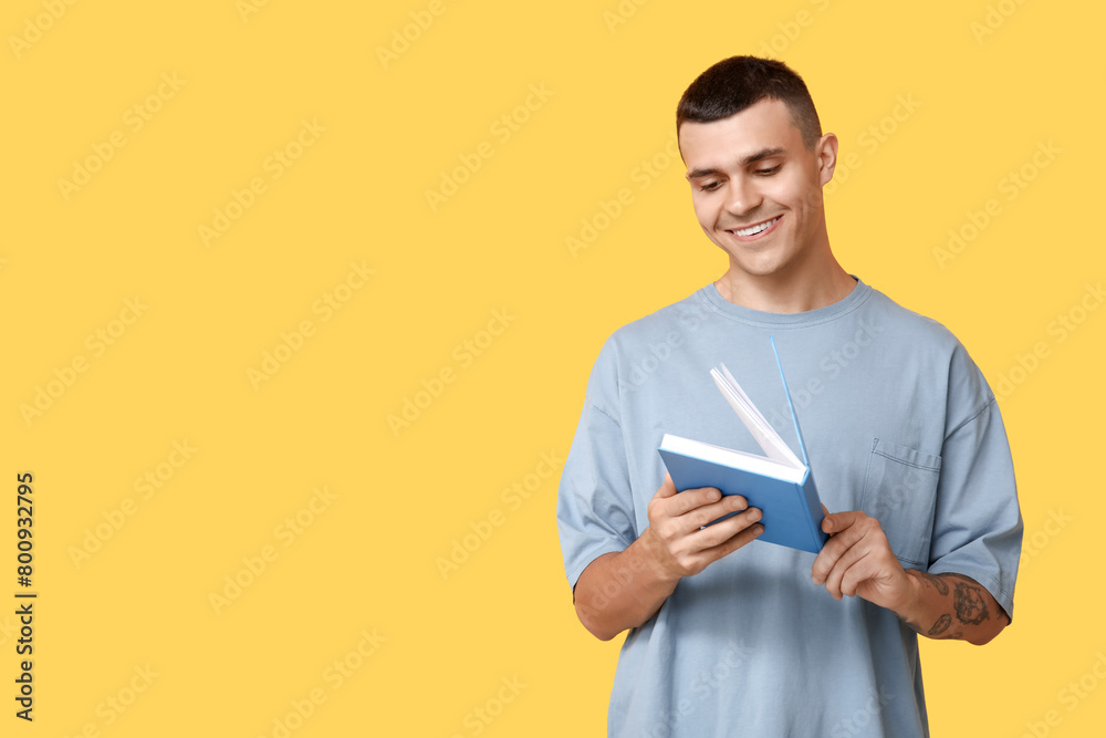 Poster Handsome young man reading book on yellow background