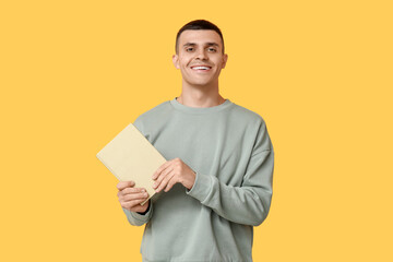Handsome young man with book on yellow background