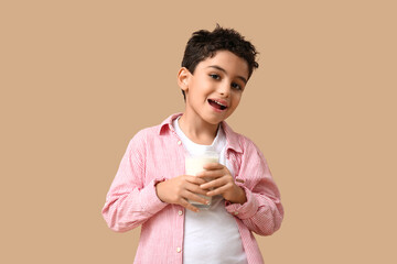 Cute little boy with glass of milk on beige background