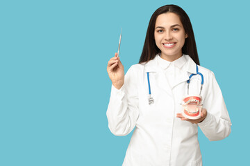 Portrait of female dentist with dental mirror and jaw model on blue background