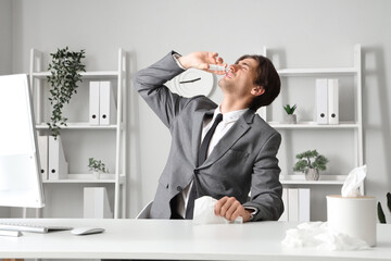 Sick businessman with tissue using nasal drops in office