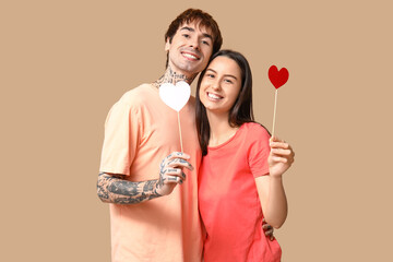 Young couple with paper hearts on beige background