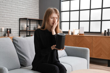 Mourning young woman with mortuary urn sitting on sofa at home