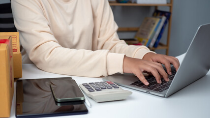 Woman runs an e-commerce business is checking orders from laptop, she owns an online store, she packs and ships through a private transport company. Online selling and online shopping concepts.