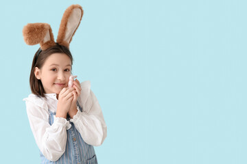 Happy little girl in Easter bunny ears with toy of rabbit on blue background