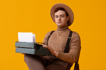 Young man with vintage typewriter on chair against yellow background