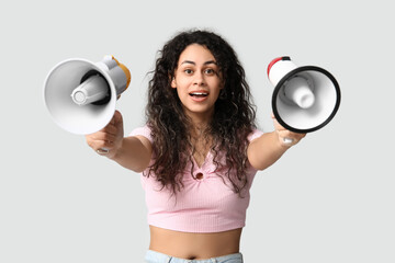 Young African-American woman with megaphones on light background