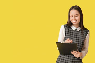 Young beautiful secretary with clipboard on yellow background