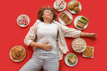 Beautiful woman with unhealthy food lying on red background, top view. Overeating concept
