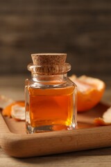 Bottle of tangerine essential oil and peeled fresh fruit on wooden table