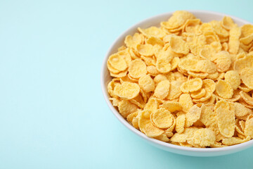 Breakfast cereal. Tasty corn flakes in bowl on light blue table, closeup. Space for text