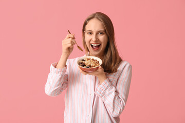 Happy young woman with bowl of healthy oatmeal on pink background
