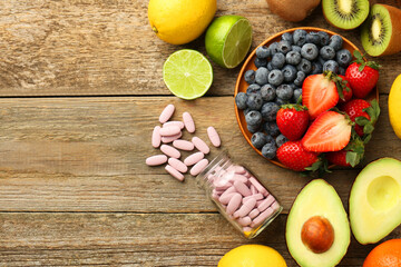 Vitamin pills in bottle and fresh fruits on wooden table, flat lay. Space for text