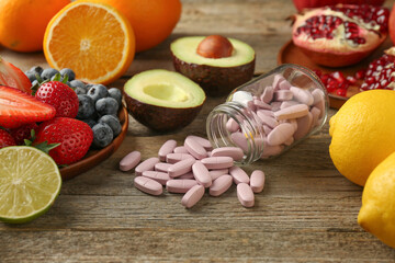 Vitamin pills in bottle and fresh fruits on wooden table