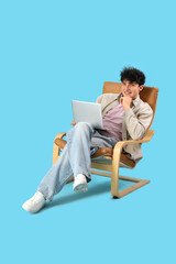 Young man resting on comfortable armchair with laptop on blue background