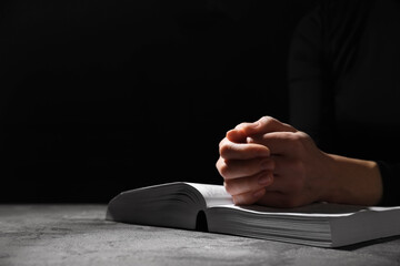 Religion. Christian woman praying over Bible at table against black background, closeup. Space for...