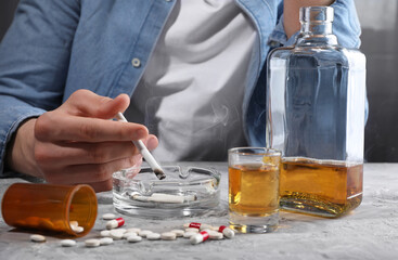Alcohol and drug addiction. Man with smoldering cigarettes, whiskey and pills at grey textured...