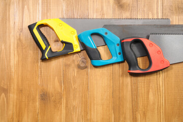 Saws with colorful handles on wooden background, flat lay. Space for text