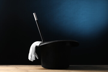 Magician's hat, gloves and wand on wooden table against dark background