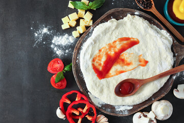 Pizza dough with tomato sauce and products on dark table, flat lay. Space for text