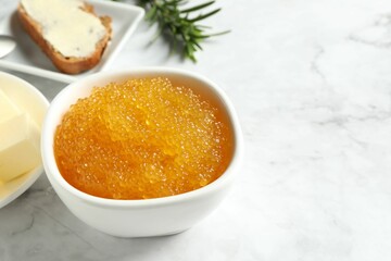 Fresh pike caviar in bowl, bread, rosemary and butter on white marble table, closeup. Space for text