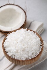 Coconut flakes in bowl and nut on light grey table