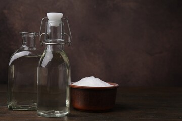 Vinegar in glass bottles and baking soda on wooden table, space for text