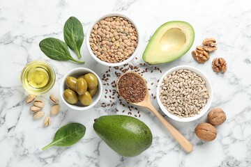 Different products and seeds high in healthy fats on white marble table, flat lay