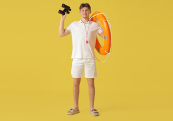 Male lifeguard with binoculars and lifebuoy ring on yellow background