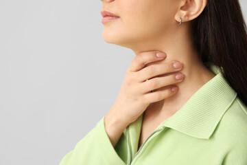Young woman suffering from sore throat on grey background, closeup