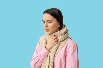 Beautiful young woman in scarf suffering from sore throat on blue background
