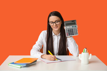 Beautiful young woman with calculator and notebooks at table on orange background