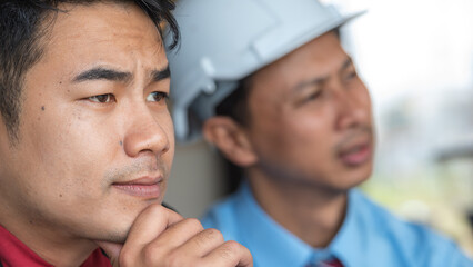 Two engineers in hard hats are looking at something thoughtfully.