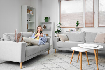 Young woman using mobile phone on sofa in light living room