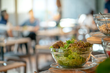 Salad bowl with lettuce, cabbage, and carrots on a wooden table in a restaurant with blurred...