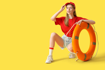 Young pretty female lifeguard in cap with rescue ring on yellow background