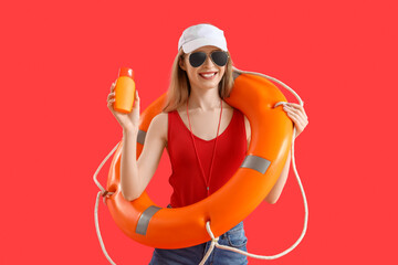 Young female lifeguard in cap with rescue ring and sunscreen on red background