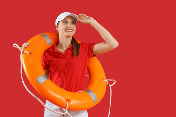 Young pretty female lifeguard in cap with rescue ring on red background