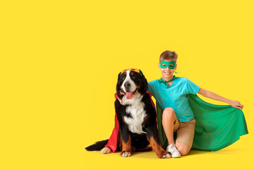 Cute fluffy dog and boy in superhero costumes sitting on yellow background