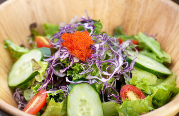 A wooden bowl with a salad of lettuce, cucumber, cabbage, and tomatoes, topped with red caviar.